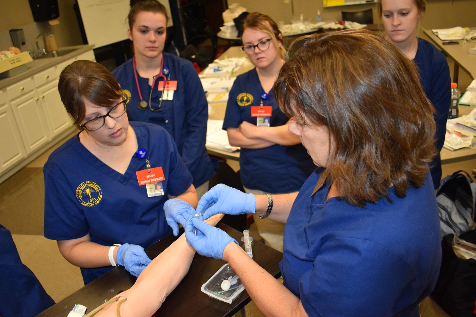 A group of nursing students practicing using needles on a training arm