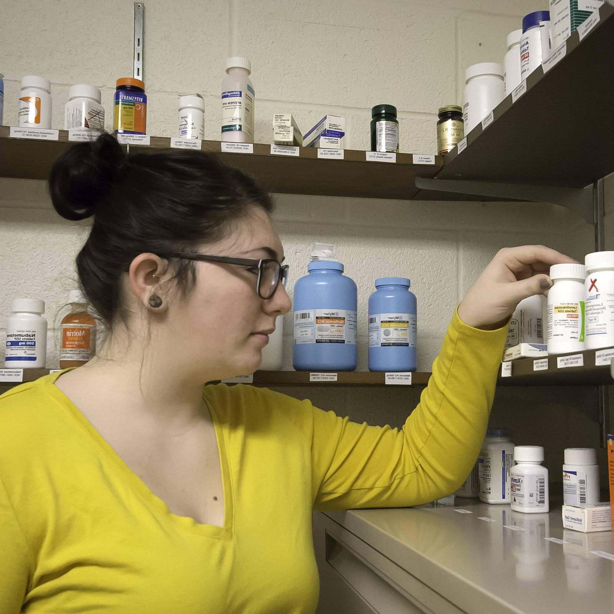 Young woman picking up a medicine bottle off of a shelf