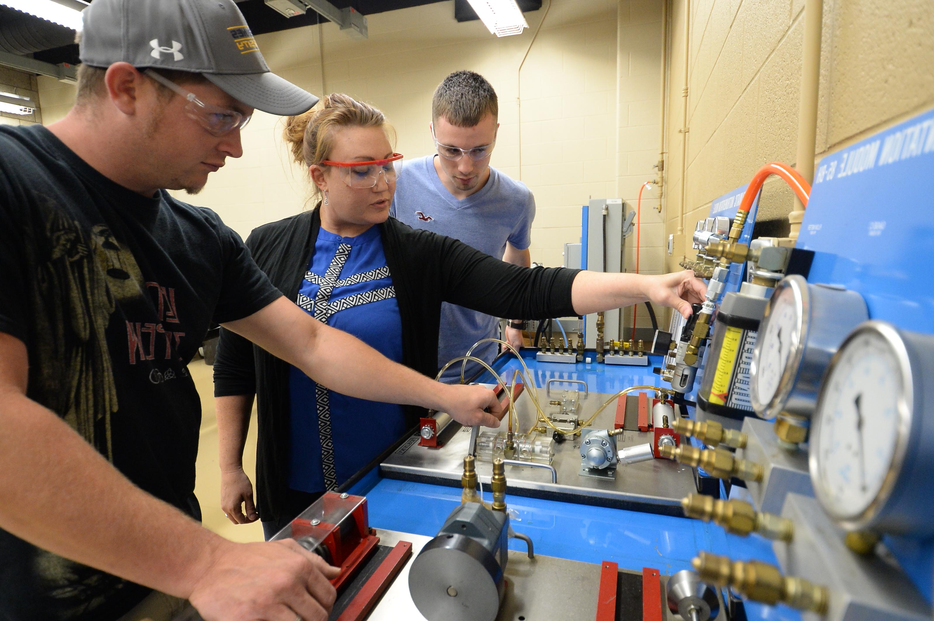 A female instructor shows two male students how to work the machinery in the shop