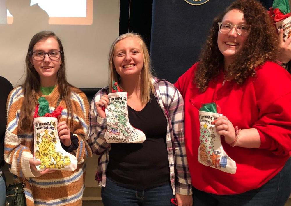 Three female students taking a photo while holding Christmas stockings